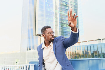 Young african businessman trying to stop a taxi in the financial district. City transportation concept.