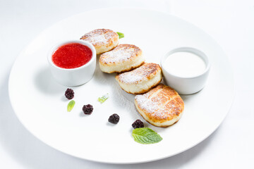 Cottage cheese pancakes, traditional Ukrainian syrniki served with sour cream and raspberry jam on white plate, healthy breakfast or brunch.