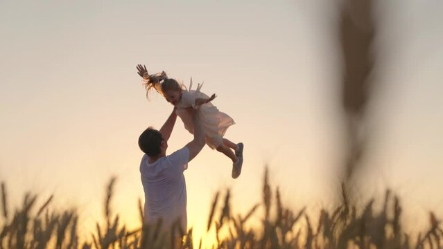 Dad plays with his daughter, throws up child with his hands in sky, outdoors. Family game concept. Childish, superhero, fly.Happy Father, child, little girl have fun together in park against sun
