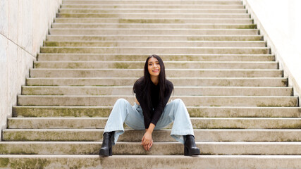 Young Colombian woman smiling sitting on urban stairs and relaxing.