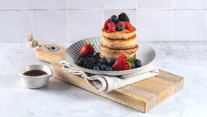 Stack of pancakes with berries on a plate on linen on a wooden board with tile background