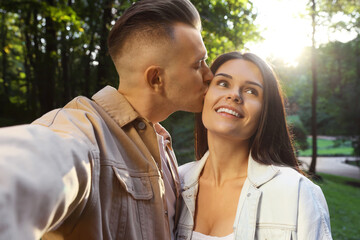 Naklejka premium Affectionate young couple kissing and taking selfie in park