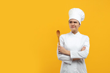 Upset female chef with wooden spoon on orange background. Space for text