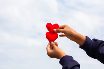 Young girl holding a heart on blur sky background. Valentine day, The child's hand gripped the red heart, lifting it into the sky.
