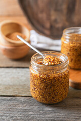 Jars and spoon of whole grain mustard on wooden table