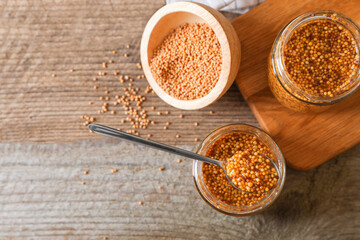 Bowl and jars of whole grain mustard on wooden table, flat lay. Space for text