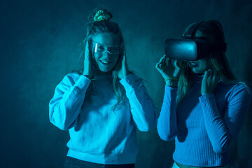 Two futuristic women in vr glasses, enjoying virtual reality, blue background