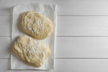 Fototapeta na wymiar Raw dough and flour on white wooden table, top view with space for text. Cooking ciabatta