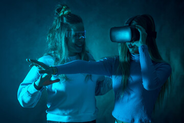 Two futuristic women in vr glasses, pointing virtual reality things, blue background