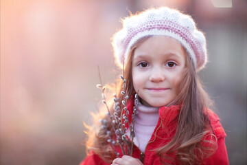 a little girl in a beret with a bouquet of willow is looking at the camera 