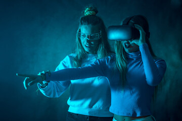 Fototapeta na wymiar Two futuristic women in vr glasses, pointing virtual reality things, blue background