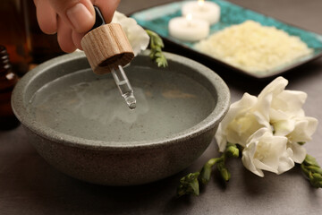 Woman dripping essential oil into bowl at grey table, closeup. Aromatherapy treatment