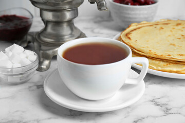 Metal samovar with cup of tea and treats on white marble table, closeup