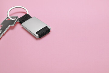 Key with metallic keychain on pale pink background, space for text