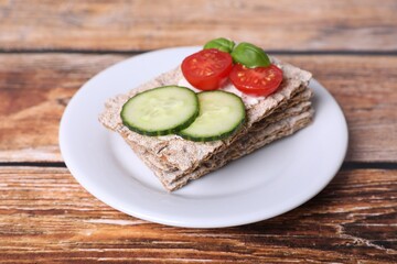 Tasty crispbreads, cucumber, tomatoes, cream cheese and basil on wooden table, closeup