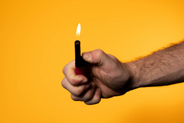 A man holding a lighter against a vibrant orange or yellow background. There is a flame coming out...