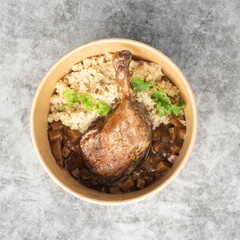 Duck leg with cauliflower rice in a kraft delivery bowl on a grey table background