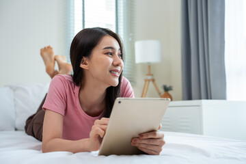 Asian attractive woman using tablet chat on bed at home in the morning. 