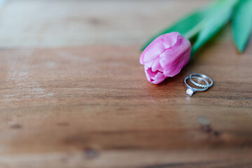 Pink tulip and a ring with a diamond lies on a wooden background. Background for Valentine's Day