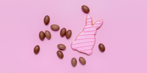 Tasty chocolate eggs and Easter cookie in shape of bunny on pink background
