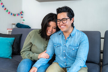 Happy gay couple sitting on sofa, positive people, with black hair in casual clothes sitting on blue couch and talking to each other in living room