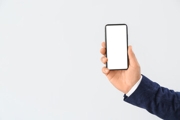 Young businessman with mobile phone on light background, closeup