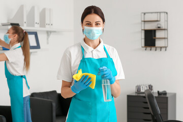 Female janitor with medical mask, rag and detergent in office
