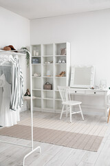 Interior of stylish dressing room with table, shelving unit and clothes