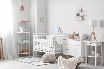 Interior of light children's bedroom with drawers, crib and table