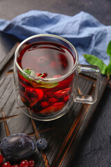 Board with glass cup of fruit tea and berries on dark background, closeup
