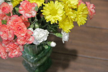 Peach and white carnations and yellow daisies bouquet in a vintage green glass flower vase, bright multicolored floral arrangement background