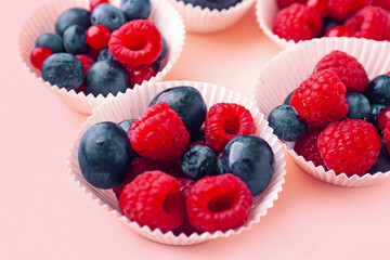 Paper baking cups with fresh berries on color background, closeup