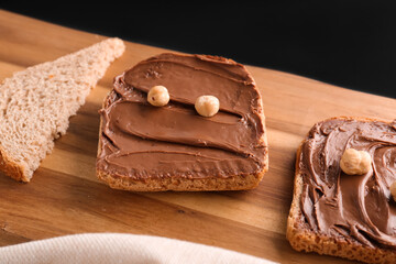 Wooden board of toasts with hazelnut butter on dark background, closeup