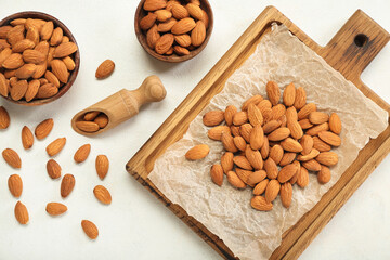 Wooden board and bowls with almond nuts on light background