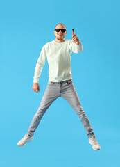 Young man in sunglasses with disposable electronic cigarette jumping on blue background
