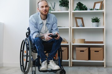 A man in a wheelchair gamer plays games with a joystick in his hands at home, surprise open mouth,...