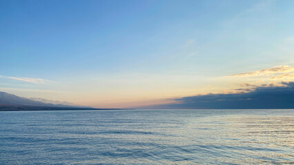Fototapeta premium Amazing panorama of a beautiful blue lake at sunset. The pearl of Kyrgyzstan is Lake Issyk-Kul. Amazing summer landscape. Calm calming natural background.