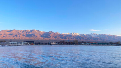 Beautiful view of the cottage settlement on the shore of Issyk-Kul Lake. Amazing panorama of a beautiful blue lake and majestic mountains at dawn.