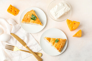 Plates with pieces of delicious cheese pie, parsley leaf, cutlery and ingredients on white table