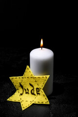 Burning candle and Jewish badge on dark background. International Holocaust Remembrance Day