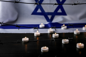 Fototapeta na wymiar Flag of Israel, barbed wire and burning candles on black wooden table, closeup. International Holocaust Remembrance Day