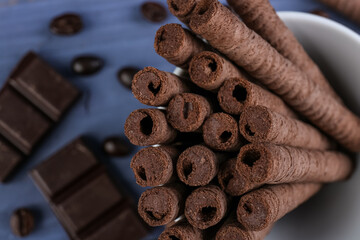 Delicious rolled wafer cookies, coffee beans and chocolate pieces on blue background