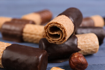 Delicious wafer rolls and hazelnuts on blue background, closeup