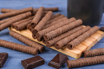 Board of delicious rolled wafer cookies with chocolate pieces on blue background