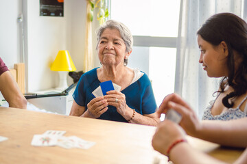 Latin grandmother analyzing her opponent in a card game in her living room.