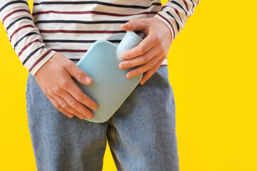 Young man with hot water bottle on yellow background, closeup © Pixel-Shot