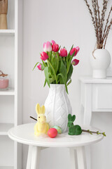 Vase with tulips, Easter eggs and rabbits on table in living room