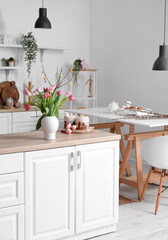 Vase with tulips, Easter eggs and cakes on counter in interior of kitchen