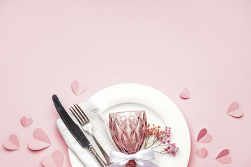 Table setting for Valentine's Day with glass and hearts on pink background