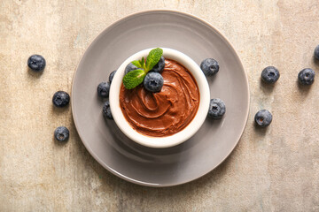 Plate with bowl of delicious chocolate pudding and blueberry on grey table